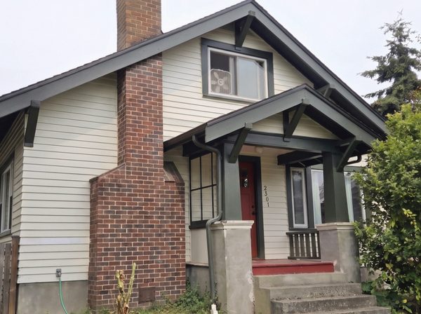 Same bungalow after repainting, off-white siding with dark green trim and a red door
